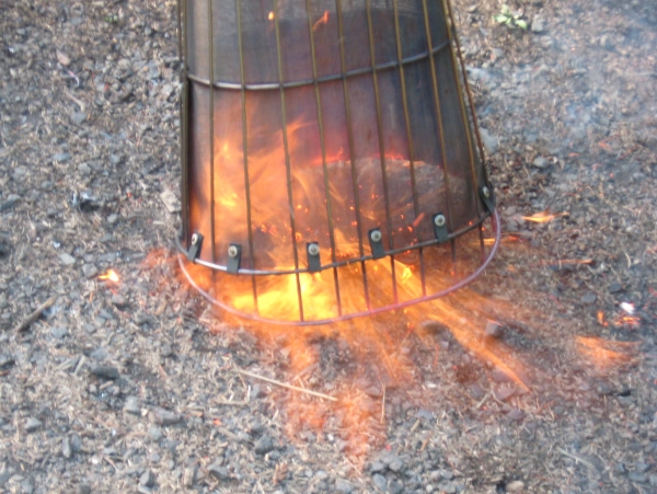 Oval basket containing heat and directing flame down to ground and forward.